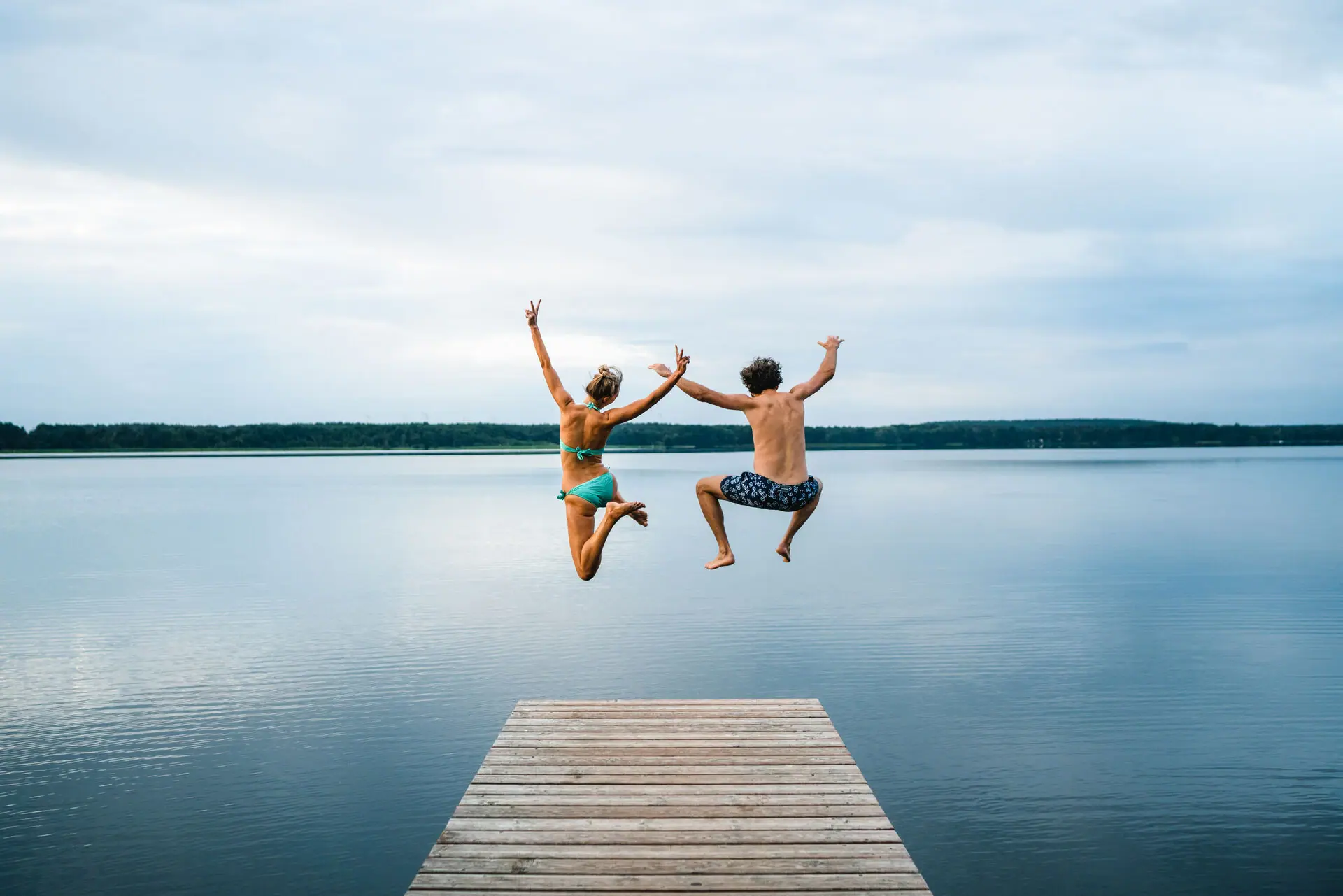 Een man en een vrouw springen van een steiger in een meer.