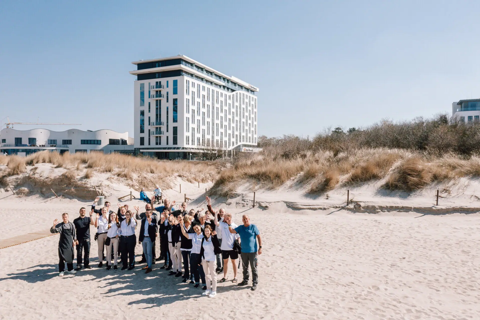 Team van de aja Warnemünde Een groep mensen van het hotelteam poseert voor een foto voor het aja Warnemünde gebouw.