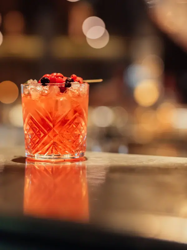 Een glas met een cocktail, gegarneerd met bessen.