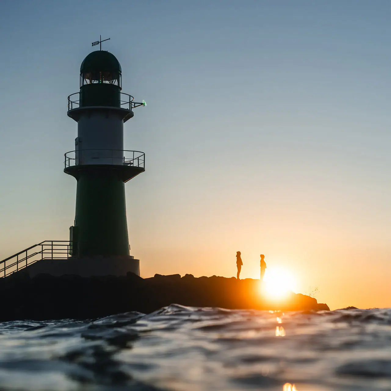 Aanbiedingen bij de aja Warnemünde Vuurtoren in het water bij zonsondergang