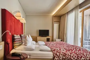 Bed met een rood-witte deken en een televisie op de achtergrond.