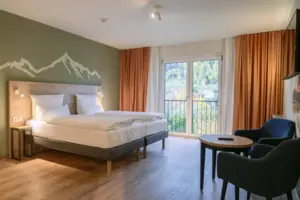Een kamer met een bed en stoelen bij een raam met uitzicht op het groen.