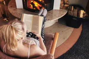 Eine Frau liest ein Buch vor einem Kamin.