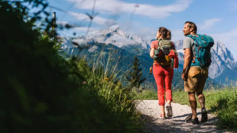 Wandelingen Garmisch Een man en een vrouw lopen over een pad met bergen op de achtergrond.