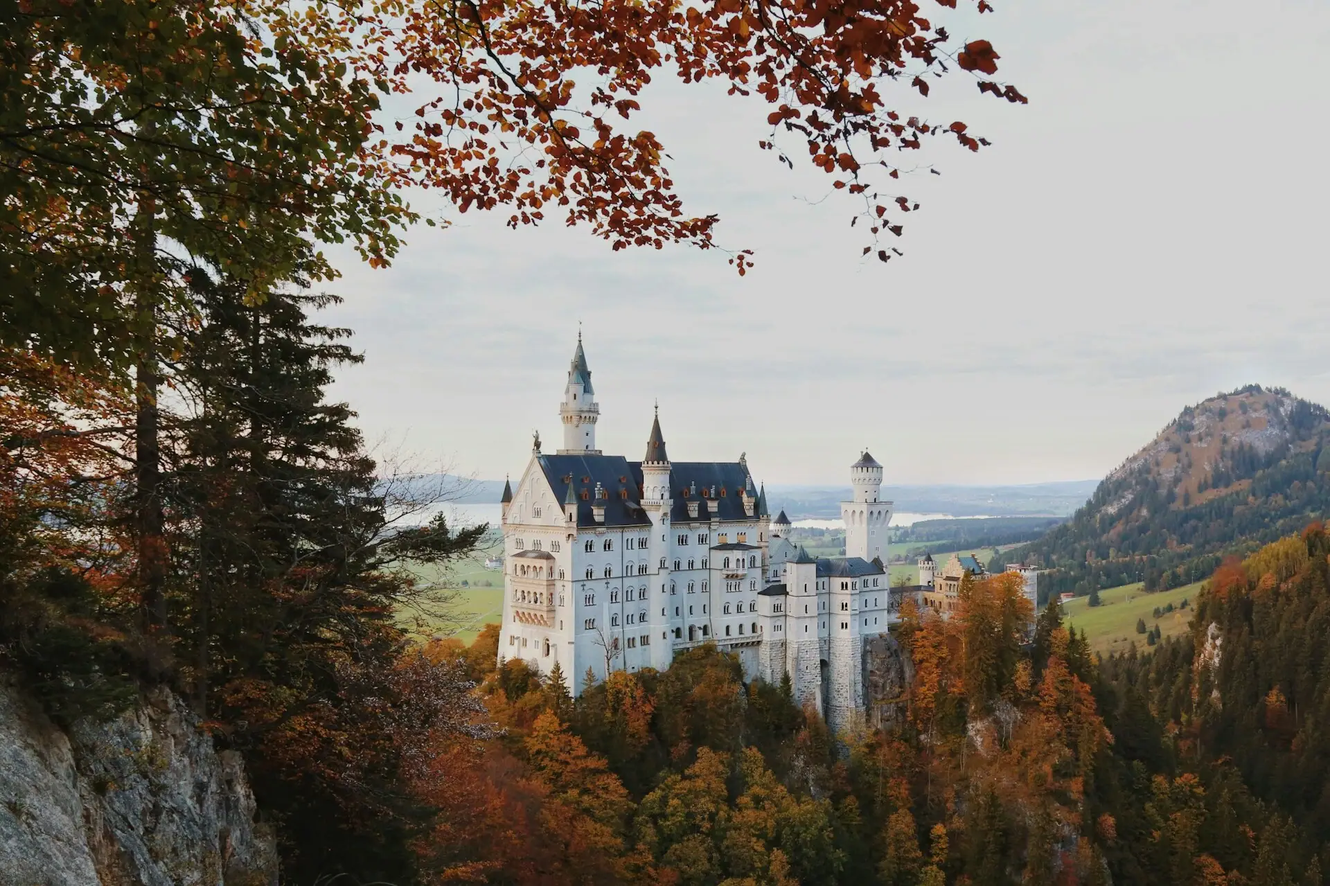 Kasteel Neuschwanstein Een kasteel op een heuvel met bomen en bergen op de achtergrond.