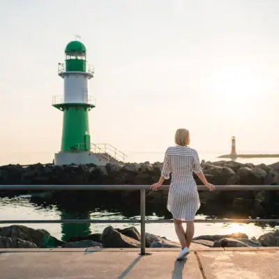 Een vrouw staat op een steiger naast een groen-witte vuurtoren.
