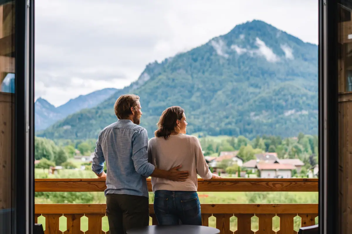 Een man en een vrouw staan op een balkon met uitzicht op een bergketen.