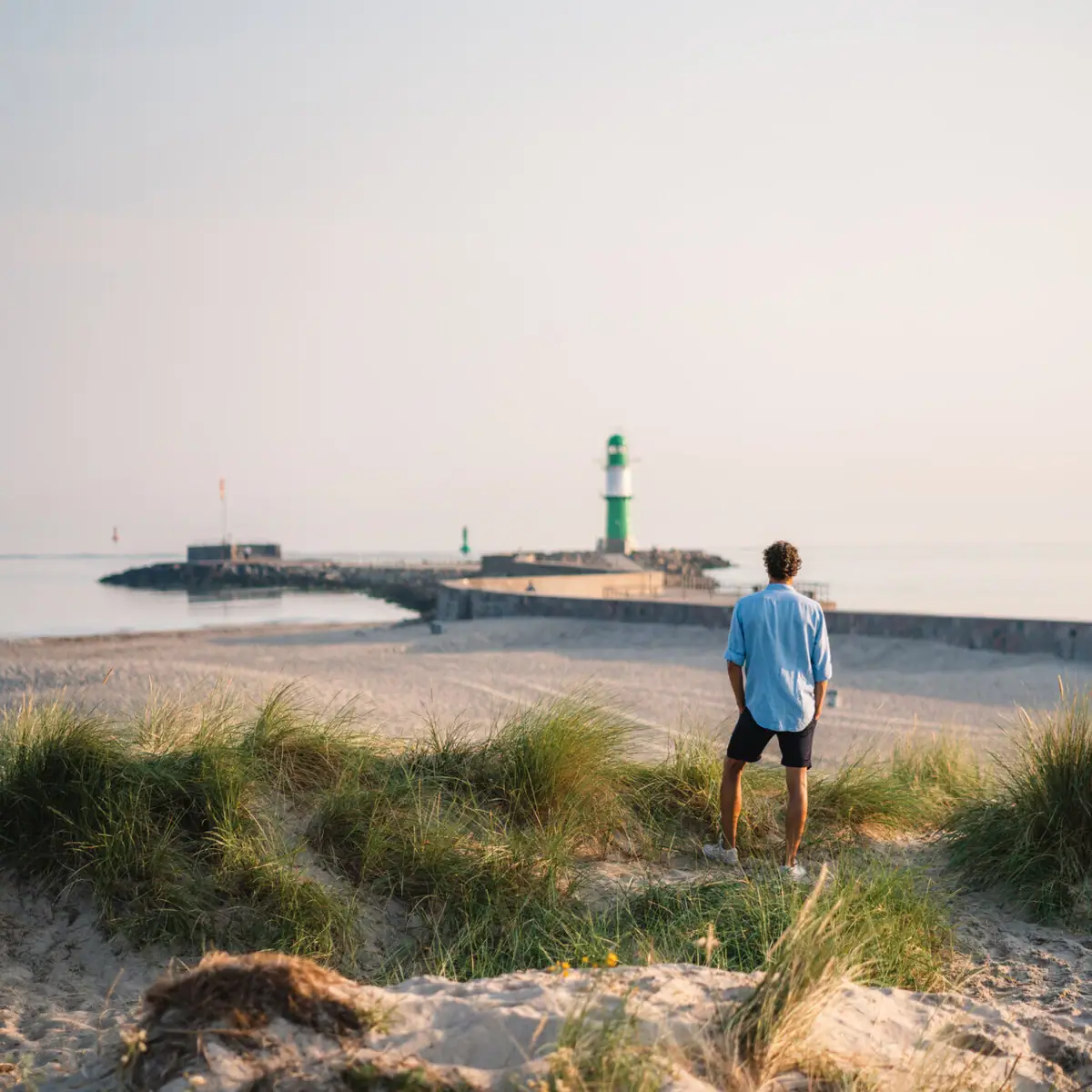 Een man staat op het strand en kijkt naar een vuurtoren.