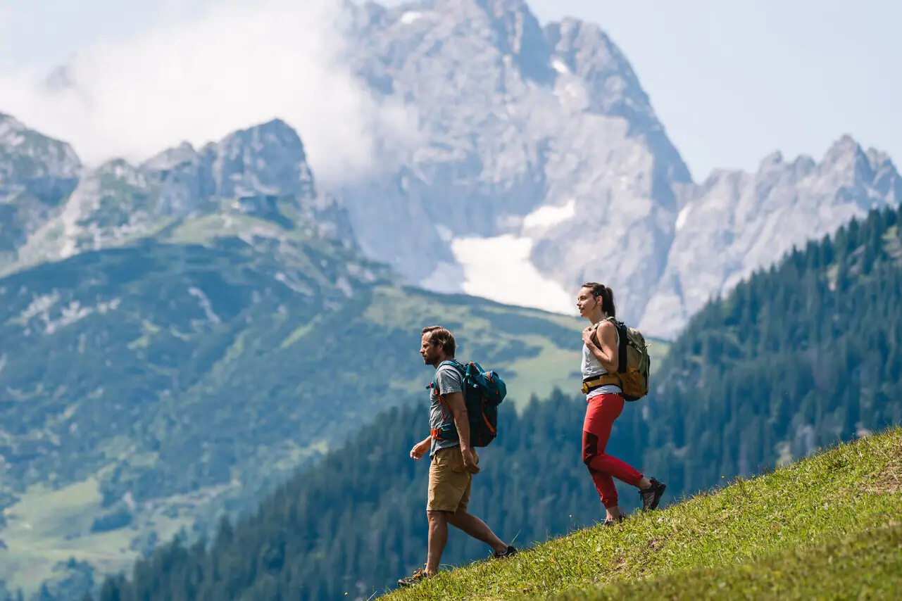 Wandelen Garmisch Twee mensen wandelen op een heuvel met bergen op de achtergrond.