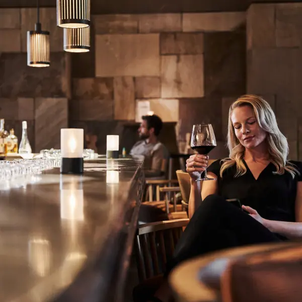 Een vrouw zit aan de bar met een glas wijn in haar hand.