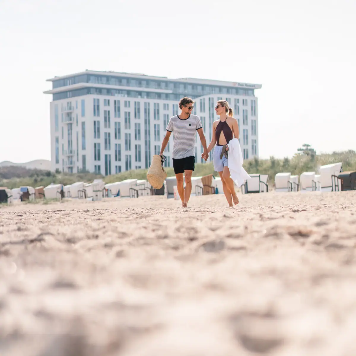 Een man en een vrouw houden elkaars hand vast op het strand.