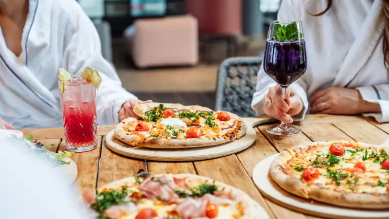 Een groep mensen zit aan een tafel met pizza's en drankjes.