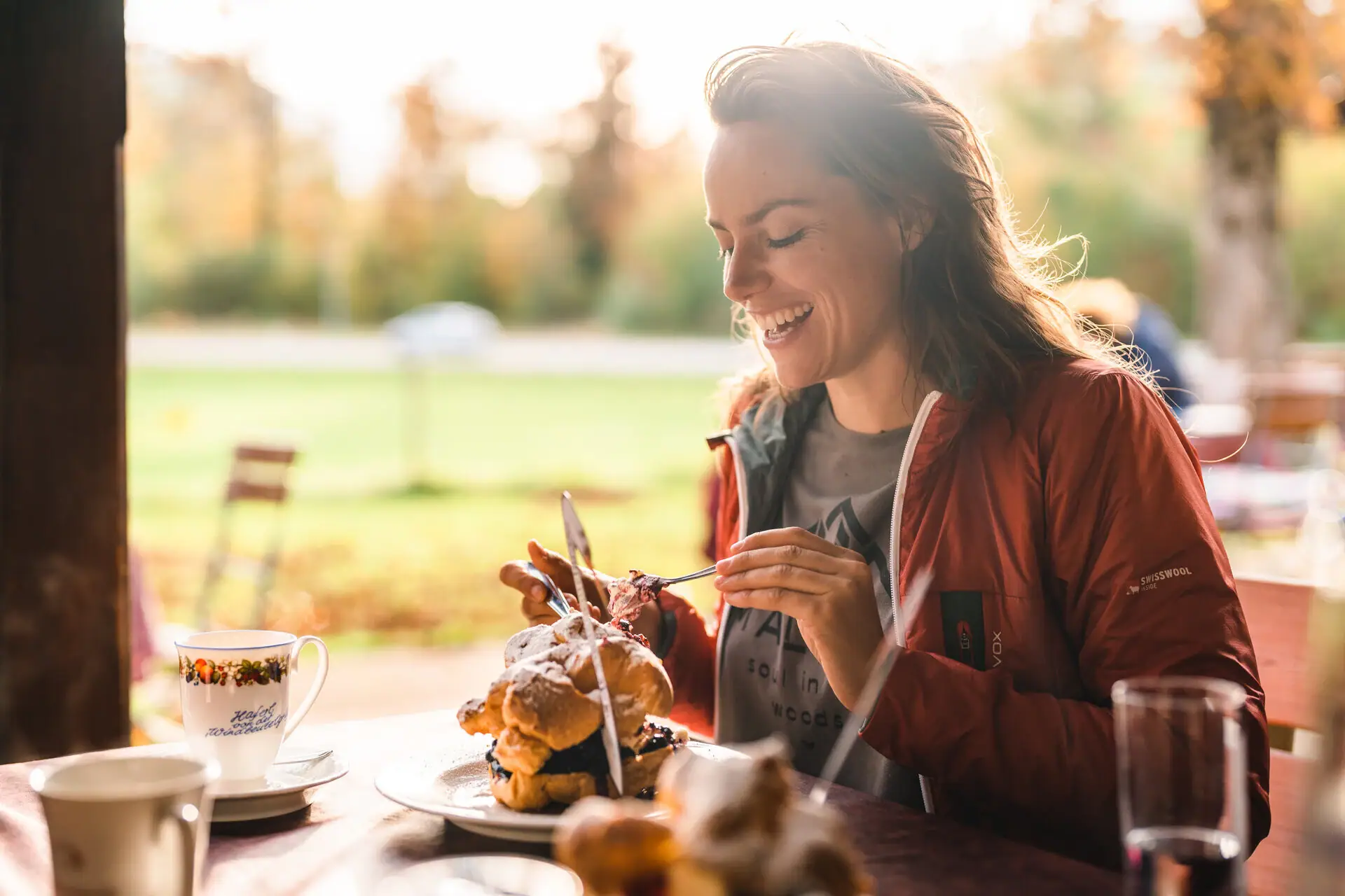 Een vrouw glimlacht aan een tafel met een roomsoes op het bord voor haar.