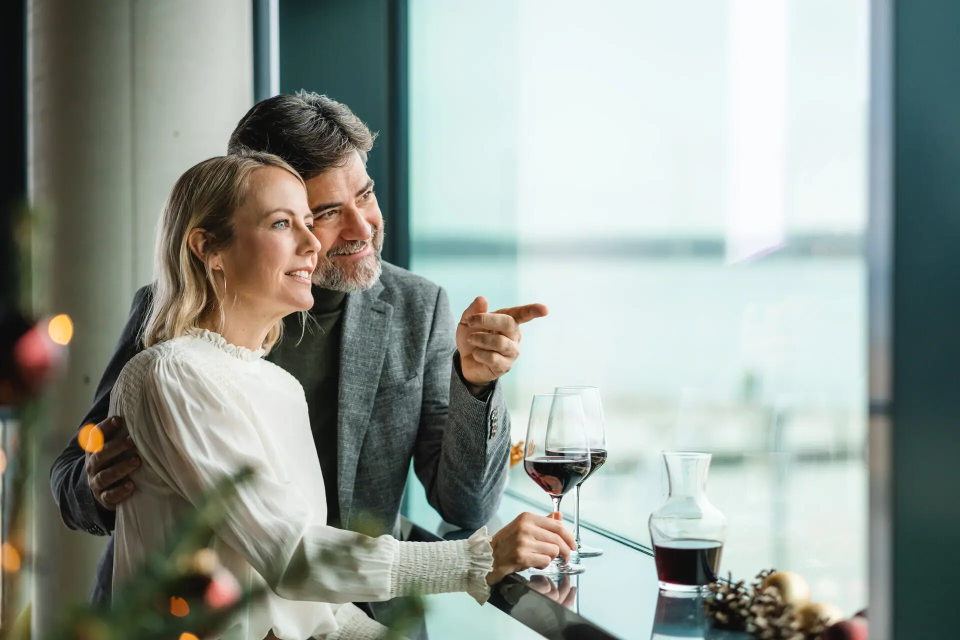 Een man en een vrouw zitten aan een bar met glazen wijn. Op de voorgrond schijnen kerstlichtjes.