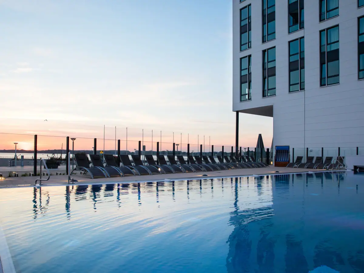 Buitenzwembad aja Travemünde Een zwembad met stoelen en een gebouw op de achtergrond.