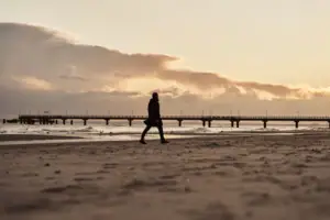 Een persoon loopt langs het strand bij zonsondergang.