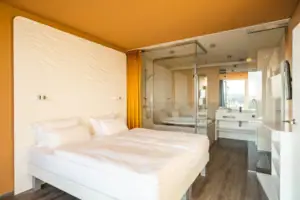 Suite bij de aja Warnemünde Een kamer met een glazen wand naar de badkamer en een bed.