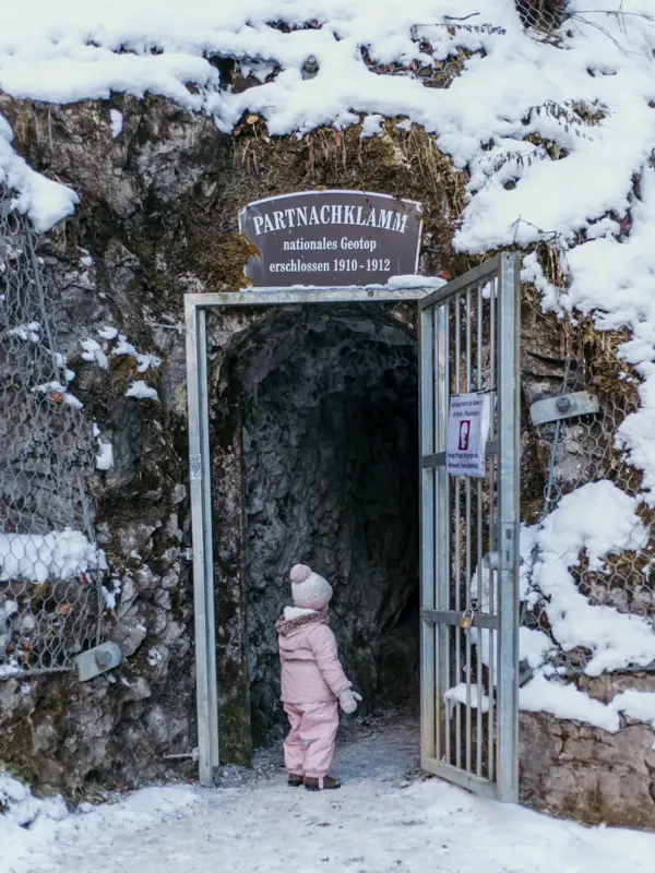 Een klein kind staat bij de ingang van de Partnachklamm tijdens een gezinsvakantie in Beieren.