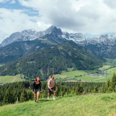 Wandelen Een man en een vrouw lopen op een heuvel, met bergen op de achtergrond.