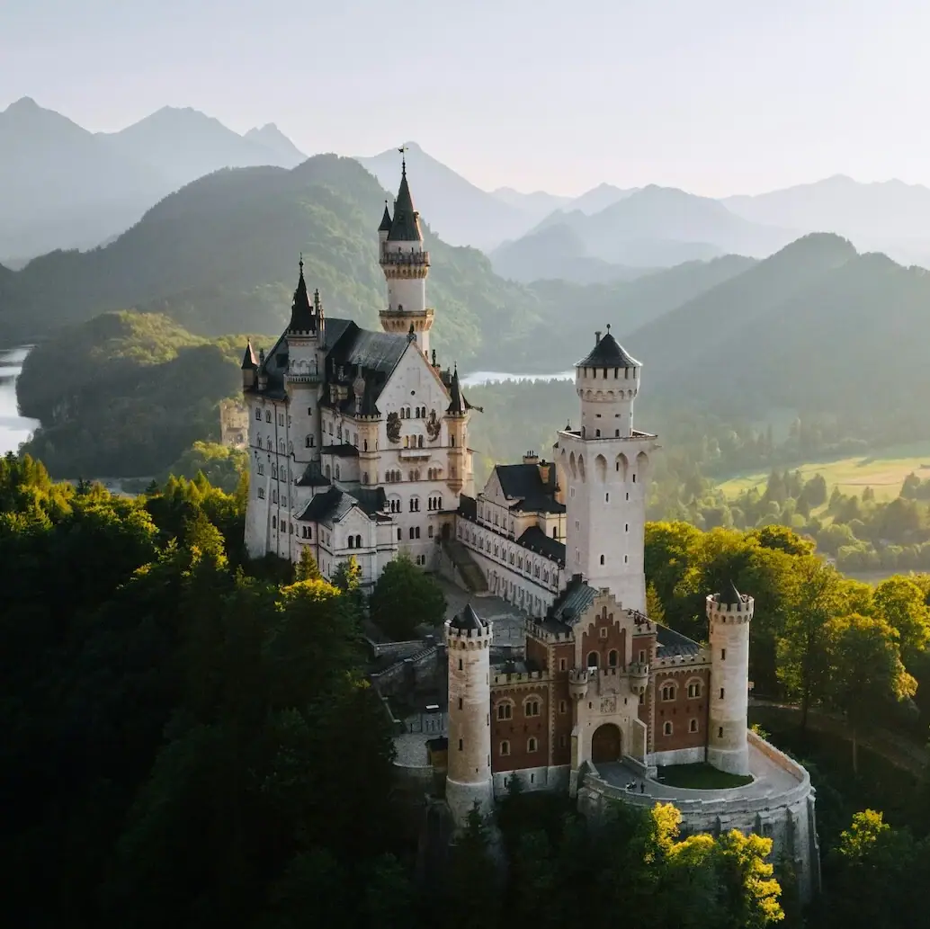 Kasteel Neuschwanstein Kasteel Neuschwanstein op een heuvel met bomen en bergen op de achtergrond.