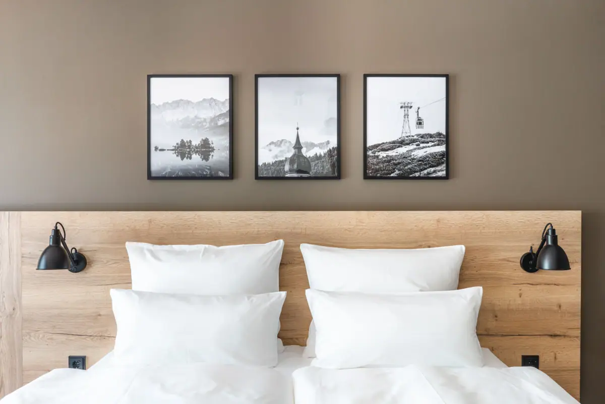 Kamer Bed met witte kussens en houten frame, op de achtergrond een foto van een berg en een skilift.