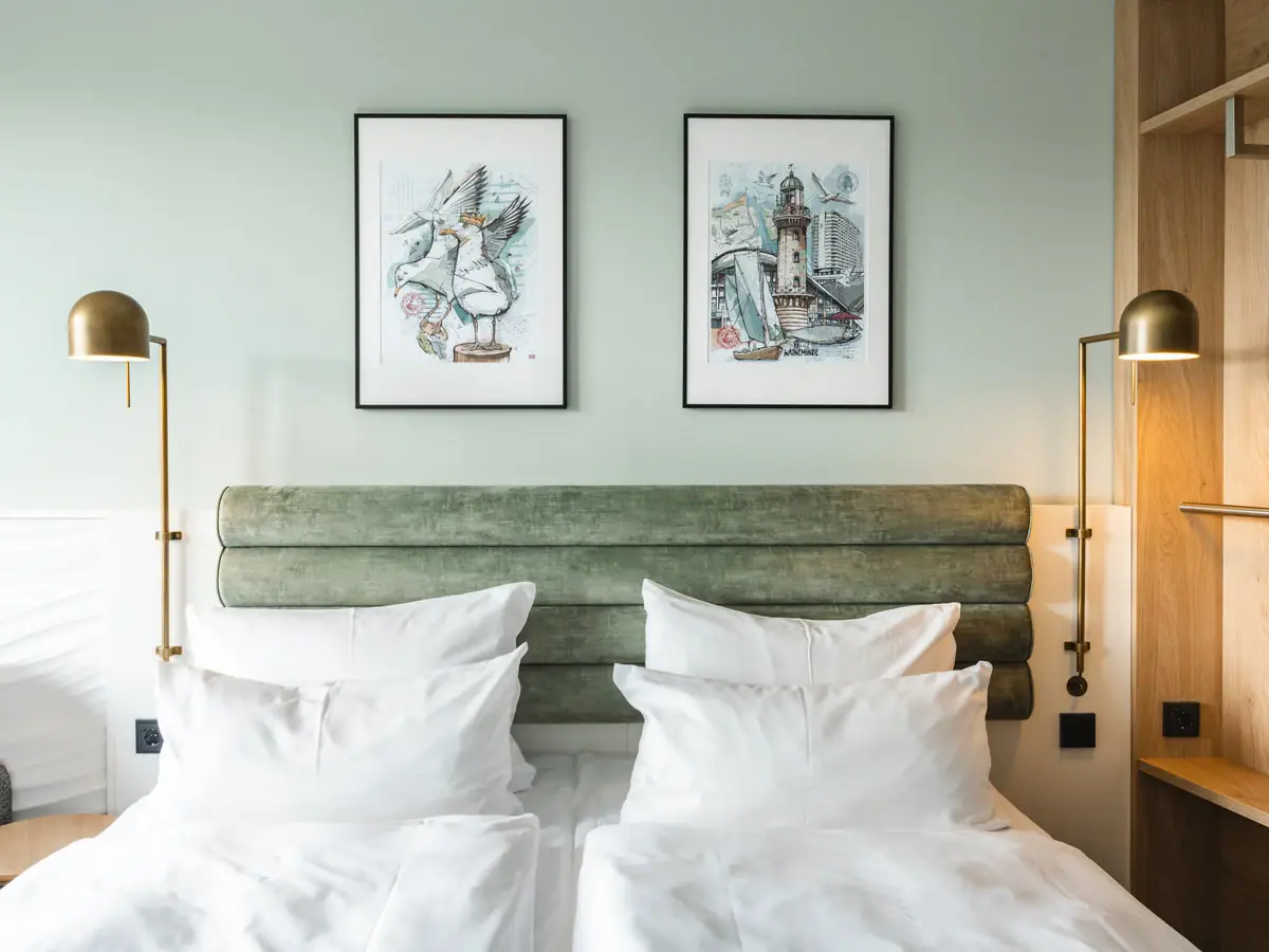 Kamer in Warnemünde Een bed met witte kussens en een groen hoofdeinde, geflankeerd door twee lampen.