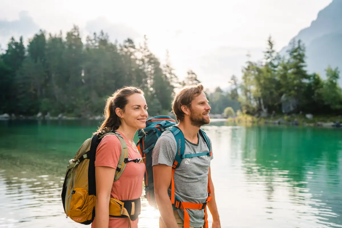 Eibsee wandeling Een man en een vrouw met rugzakken staan voor een watermassa.