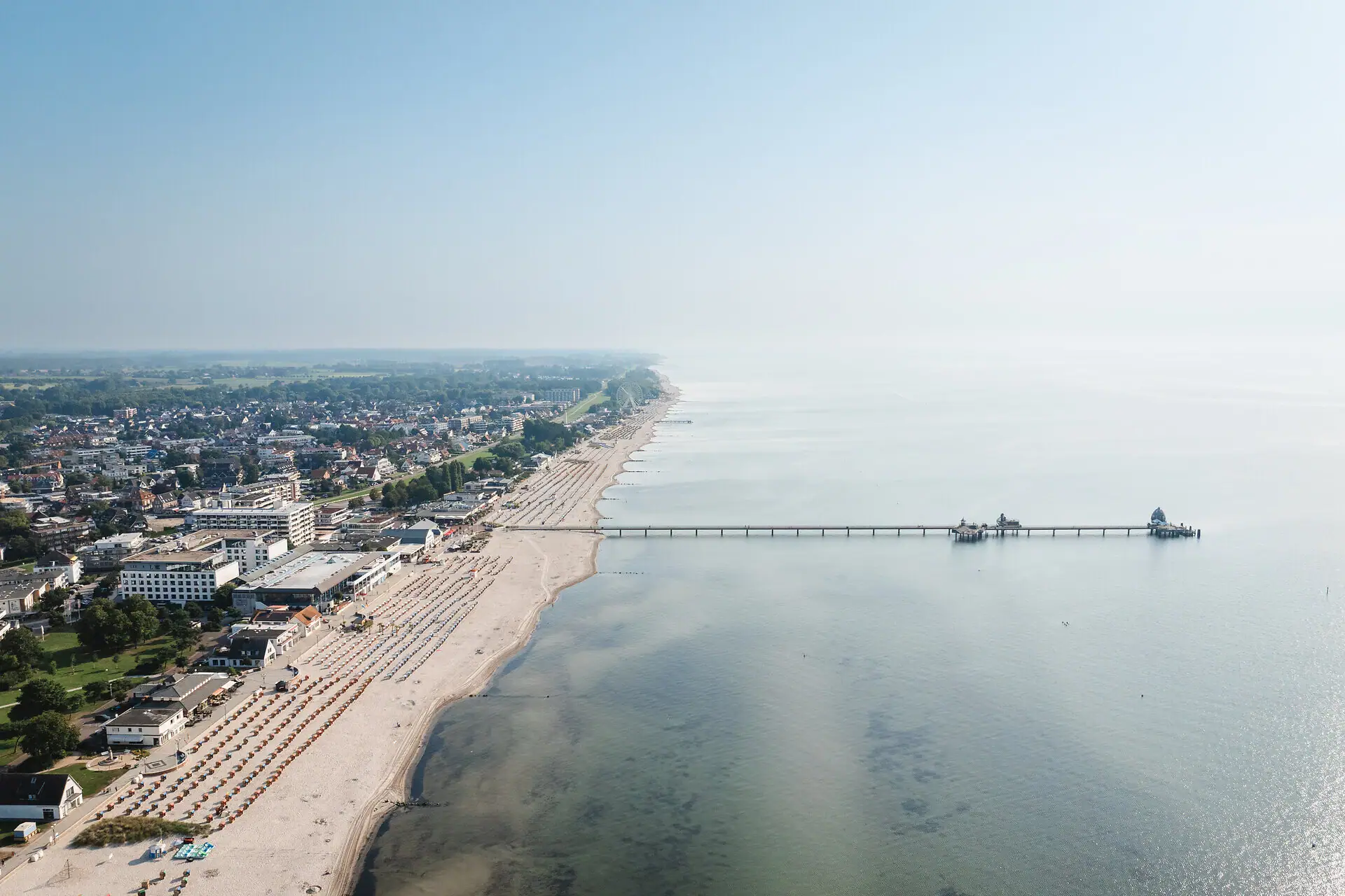 Strand met een pier en gebouwen op de achtergrond.