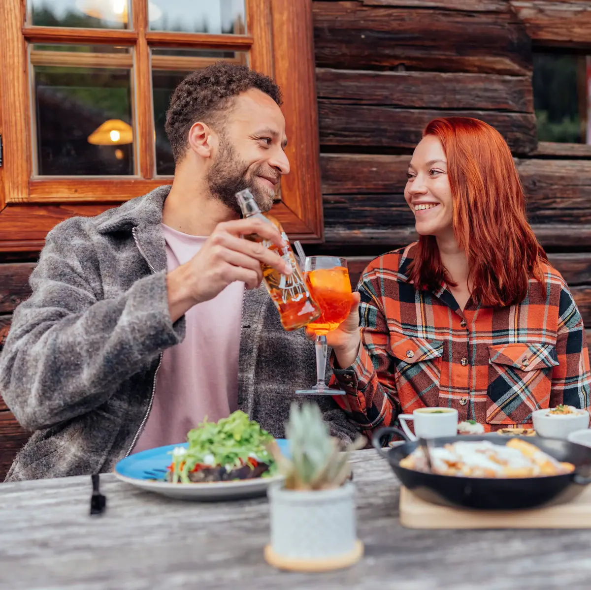 Dineren in het Stroblhaus Een man en een vrouw zitten aan een tafel te drinken; er staat wat eten en een koekenpan op.