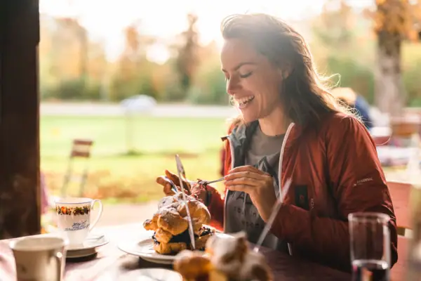 Een vrouw glimlacht aan een tafel met een roomsoes op het bord voor haar.