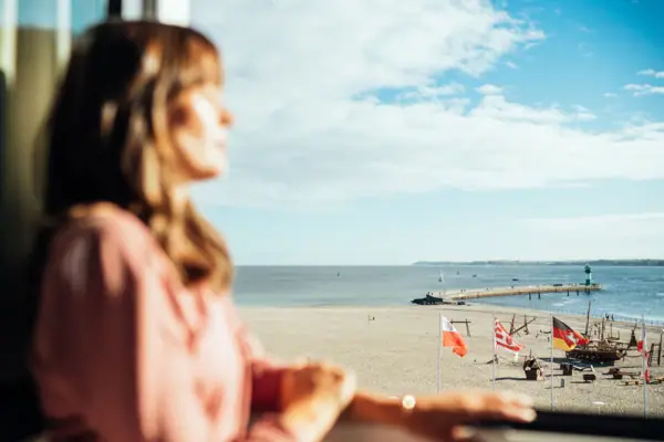 Kamer Een vrouw kijkt uit een raam op een strand.