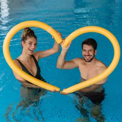 Een man en vrouw houden een gele buis in de vorm van een hart vast in een zwembad.