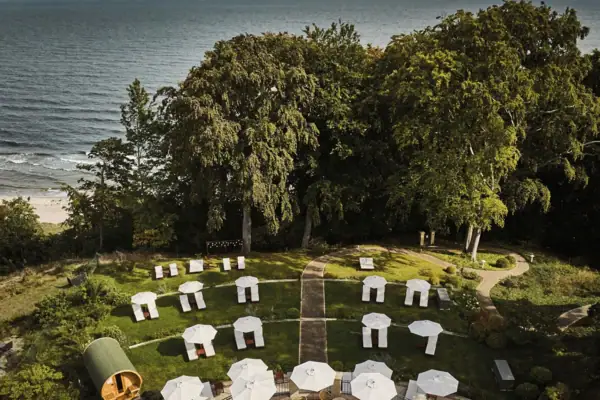 Een groep witte parasols op een grasveld met bomen en de zee op de achtergrond.