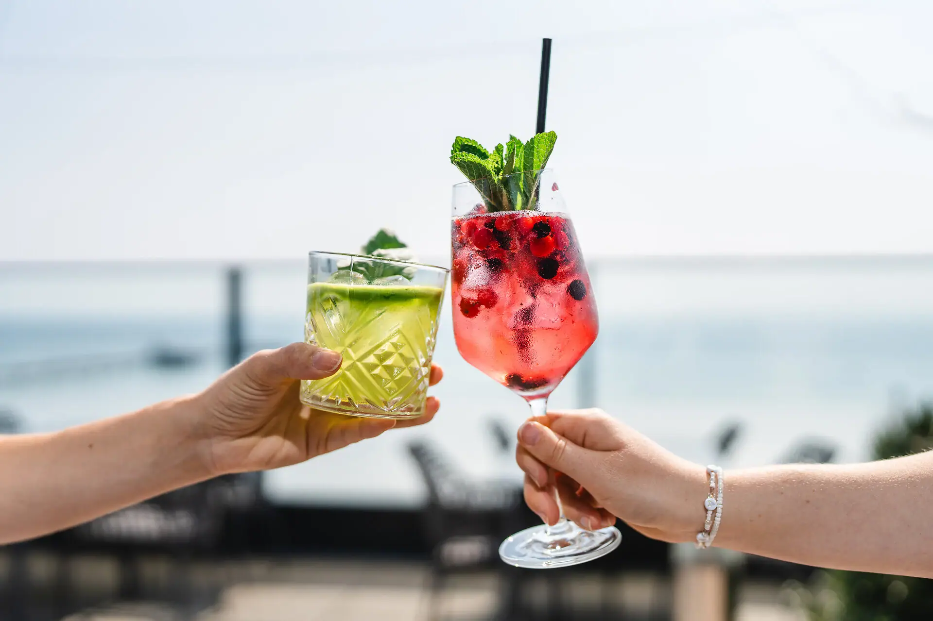 aja Bar Grömitz Een paar handen die cocktails met fruitgarnering vasthouden.