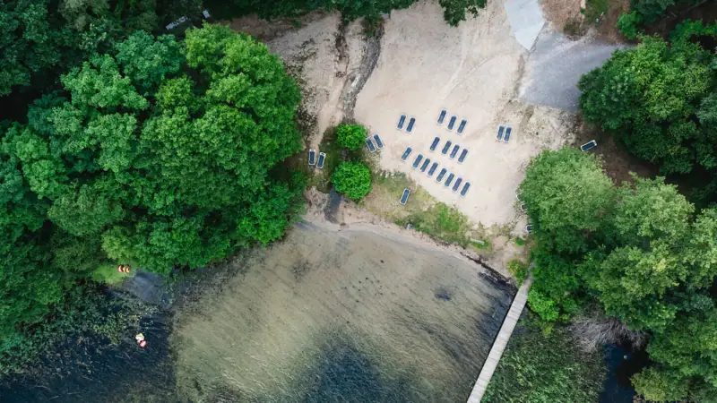 aja Bad Saarow Een loopbrug over een waterlichaam met stoelen en bomen.