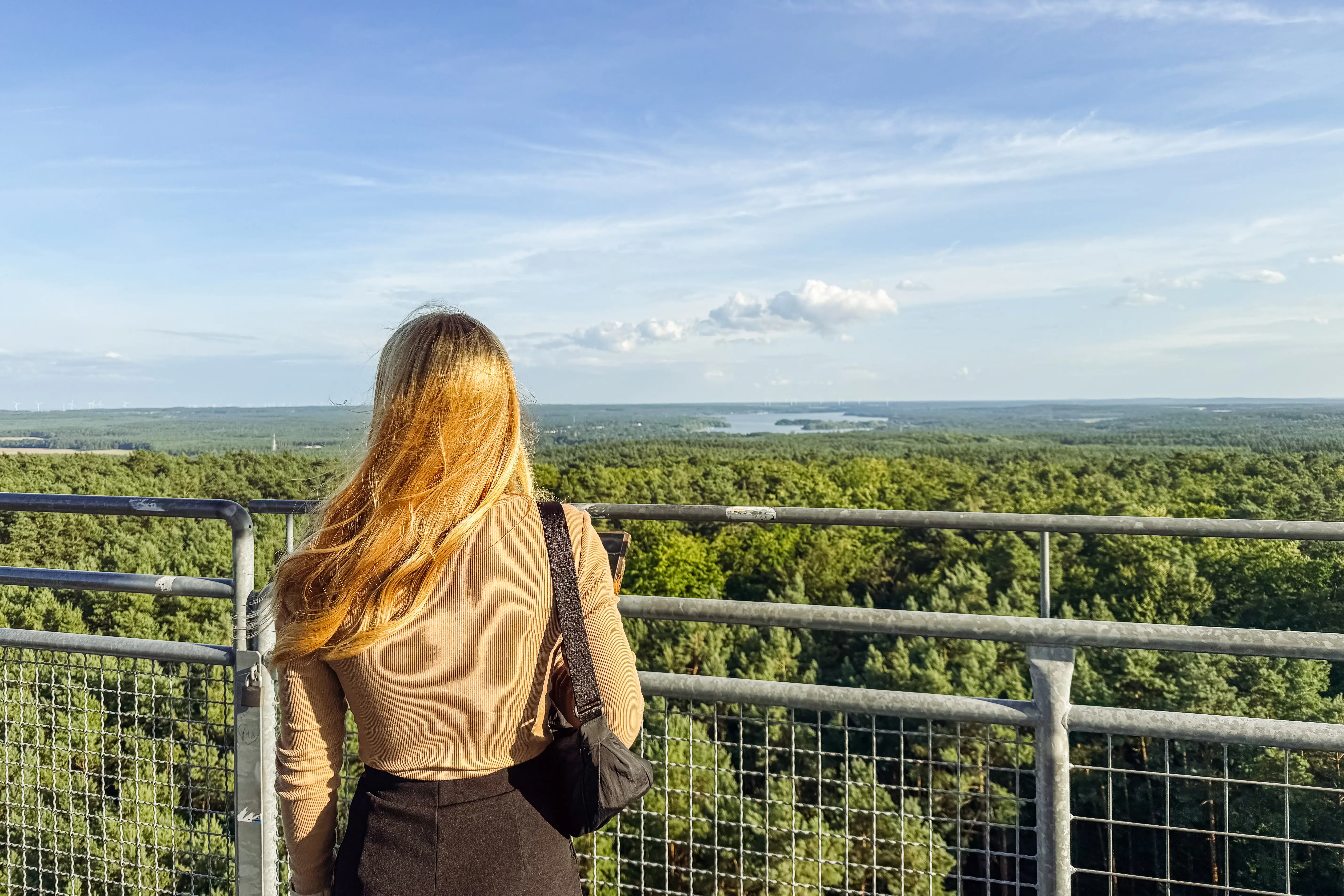 Een vrouw staat op een balkon dat uitkijkt over een bos.