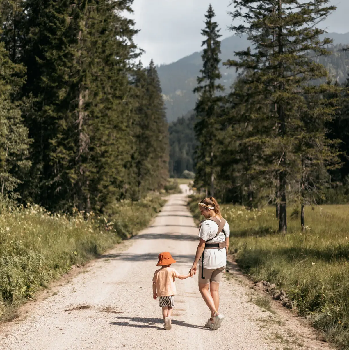Een vrouw en een kind lopen over een veldweg met bomen.