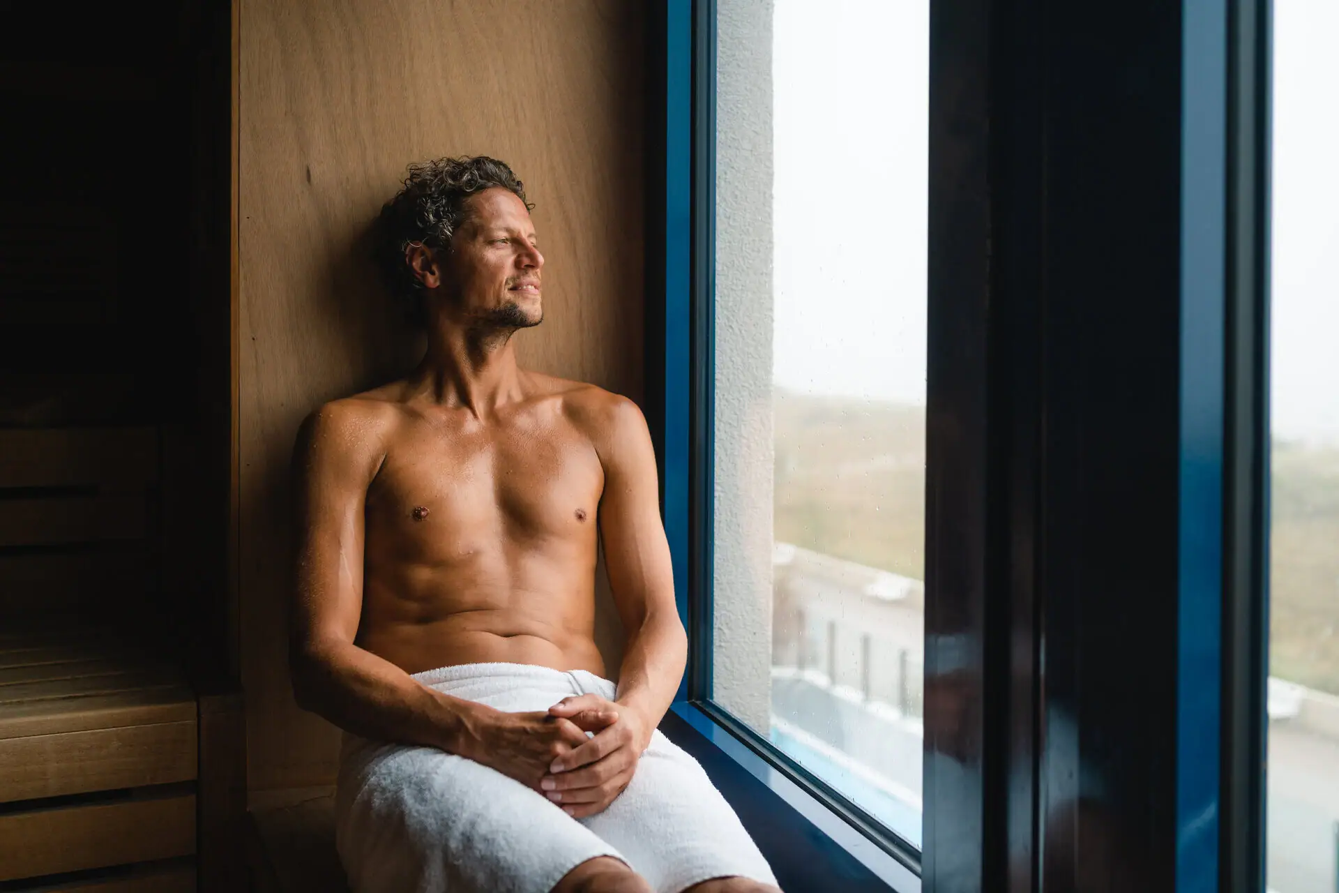 Sauna bij aja Warnemünde Een man zit op een bankje in de sauna en kijkt uit het raam.