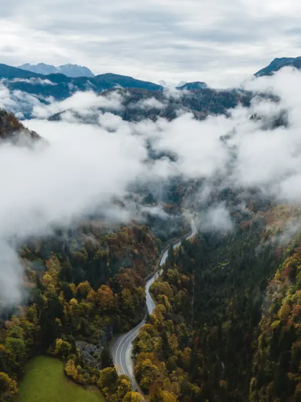 Bergpanorama Ruhpolding Een bochtige weg door een dal met wolken.