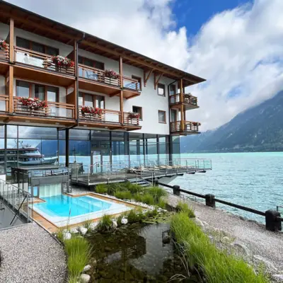aja Fürstenhaus aan de Achensee Een gebouw met een zwembad en een waterpartij op de voorgrond.
