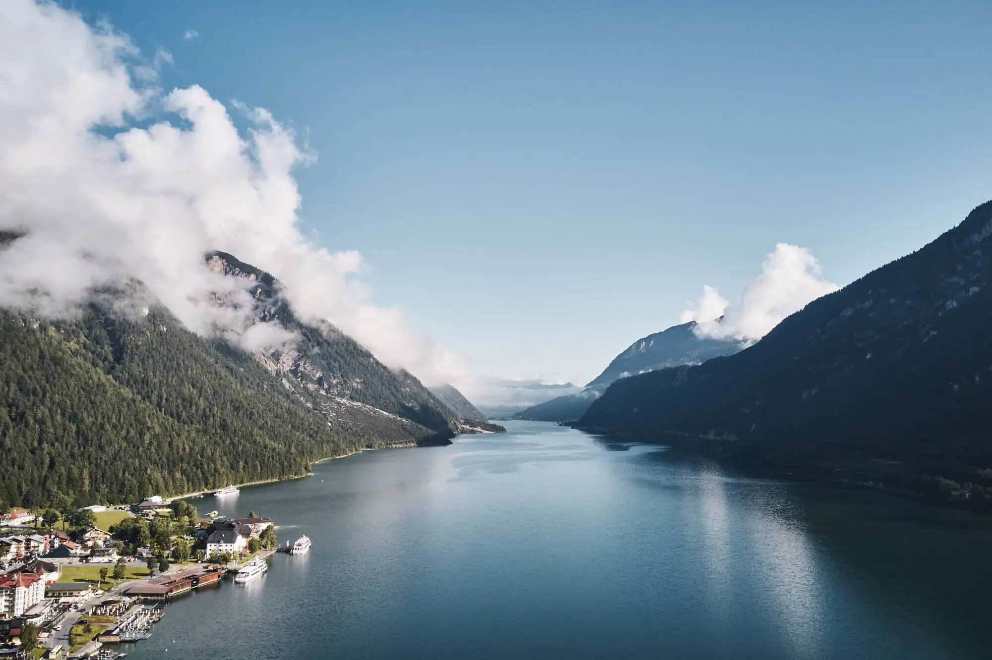 Achensee Meer Een waterlichaam met een huis en bergen op de achtergrond.