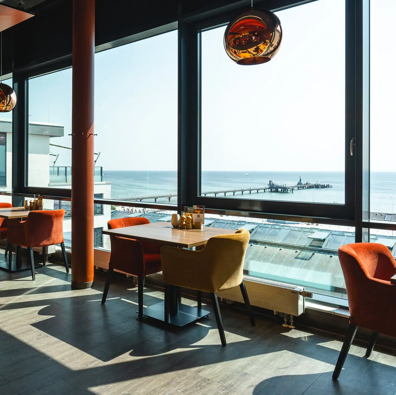Het aja restaurant in Grömitz met tafels en stoelen en een raam met uitzicht op de Oostzee en de pier.
