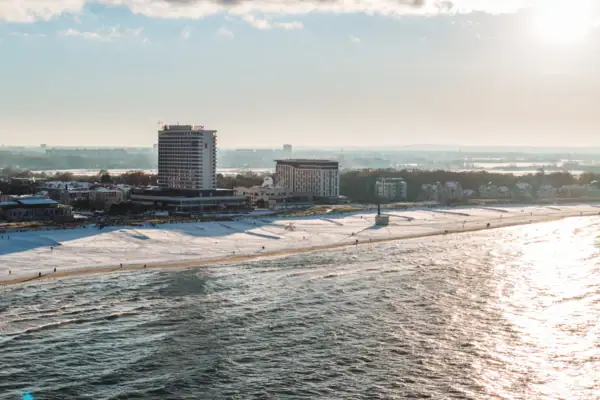 Strand mit dem aja Warnemünde und Schnee im Vordergrund, bewölkter Himmel im Hintergrund.