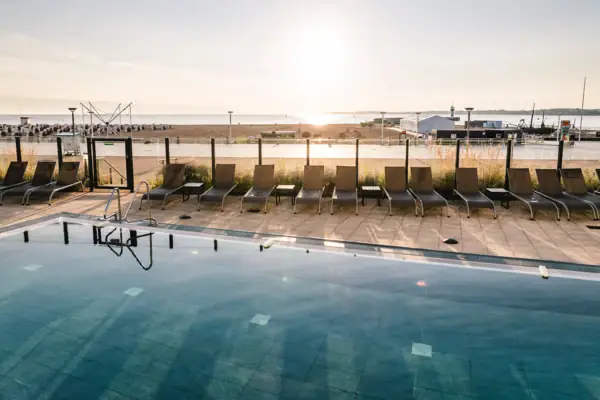 Een zwembad met stoelen en een strand op de achtergrond.