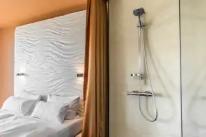 Suite bij de aja Warnemünde Douchekop en glazen wand, op de achtergrond het bed in een slaapkamer.