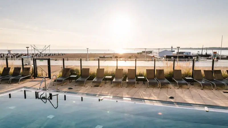 Een zwembad met stoelen en een strand op de achtergrond.