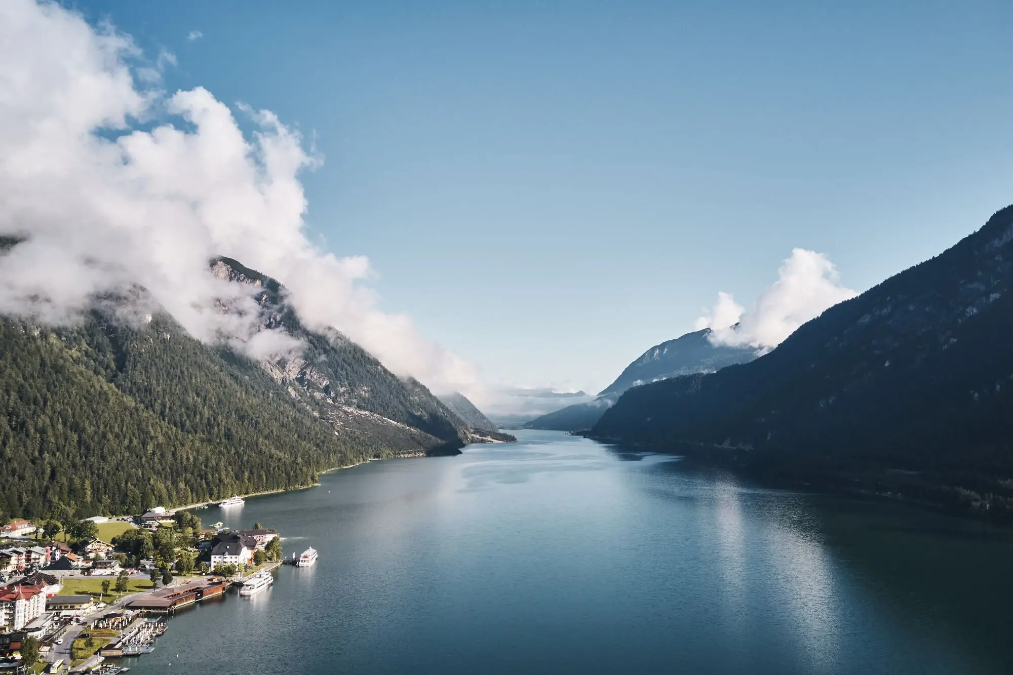 Achensee Meer Een waterlichaam met een huis en bergen op de achtergrond.