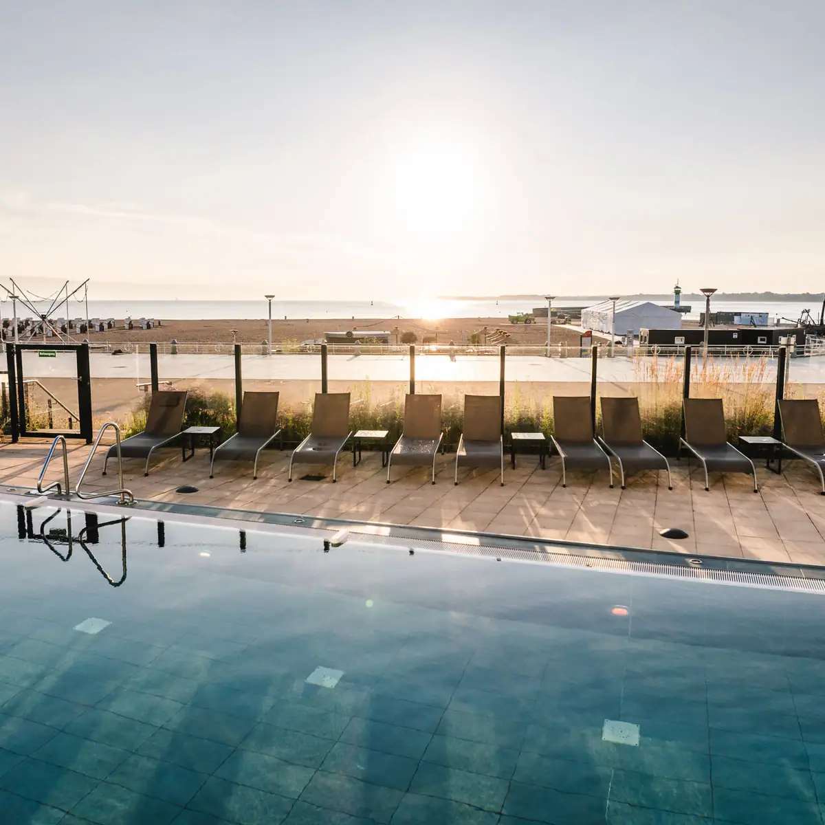 Buitenzwembad met uitzicht op het strand Een zwembad met stoelen en een strand op de achtergrond.