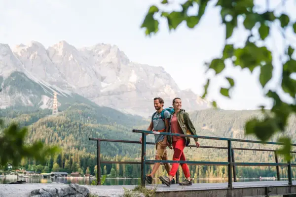 Wandelen Een koppel wandelt op een brug met een meer en bergen op de achtergrond.