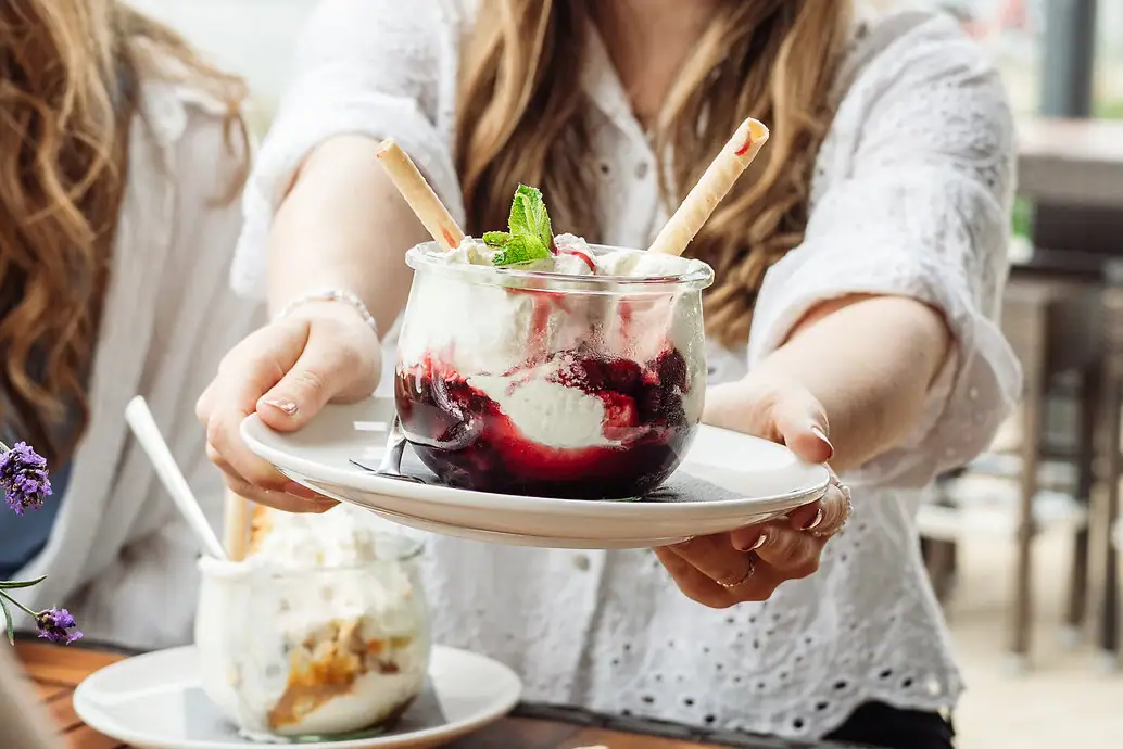 Een vrouw houdt een bord vast met een sundae met vanille-ijs en kersen.